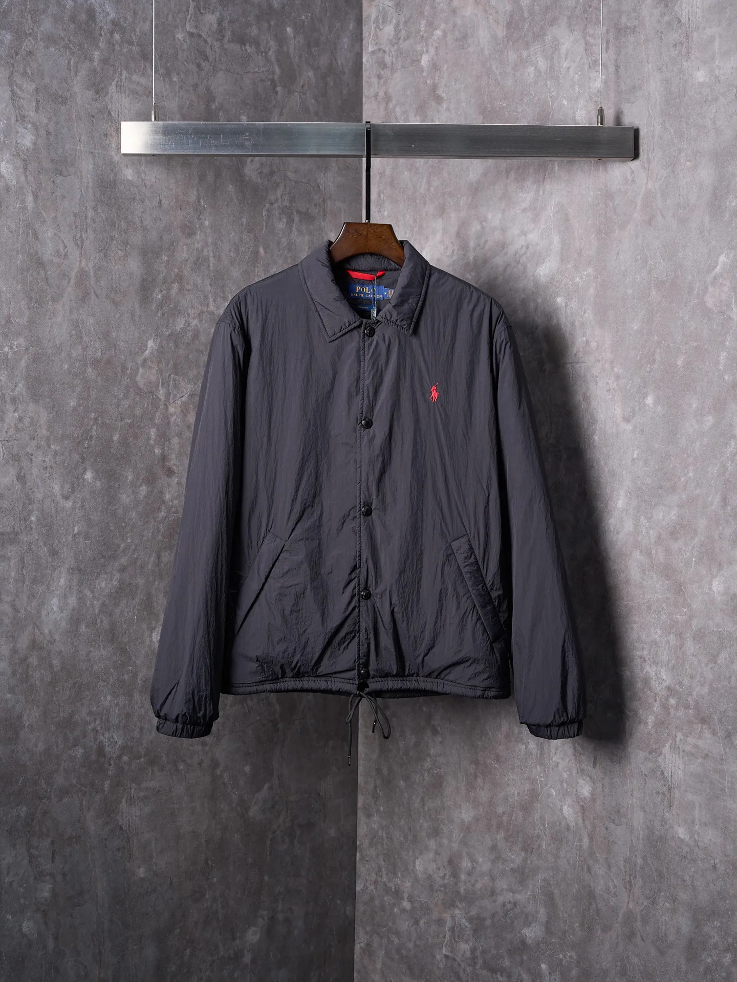 P640 Actual auction] Ralph Lauren/Ralph Lauren Pony Red Label lightweight cotton lapel coach jacket [Ready stock] S M L XL Material: high-density nylon taffeta Features: Density is about 210T-300T, smooth and slightly matte surface, excellent windproof and waterproof performance (with DWR water-repellent treatment), strong wrinkle resistance and easy care, in line with the positioning of American casual "durable and practical".  Color: Classic dark black, using vat dyeing process (dye penetrates into the fiber), the color fastness reaches ISO level 4 or above to avoid fading or color transfer after washing.  2. Lining fabric Material: Lightweight cotton-polyester blended lining (65% Polyester + 35% Cotton) Function: Reduce friction between the fabric and inner clothing, improve wearing smoothness; blended material has both breathability and durability to avoid the stuffy feeling of pure nylon lining.  Version and cutting process Version: Classic Coach Jacket, loose version, slightly dropped shoulder line (shoulder width is 1-2cm wider than the standard version), length to the hips, and slightly tapered straight sleeves, taking into account both freedom of movement and casual style. Embroidery technology: Polo horse logo on the left chest: flat satin stitch embroidery (satin embroidery), embroidery thread: 100% polyester high color fastness embroidery thread (the color number is consistent with the brand’s standard red color card), stitch density 12-15 stitches/cm, the outline of the horse logo is clear, and the details of the rider and horse are burr-free.  Embroidery positioning: precise positioning through the template (12cm from the neckline and 8cm from the placket) to ensure left and right symmetry and centering.  Topstitching technology: The seams of the body are made of double-needle flat seams (needle pitch 3cm/10 needles), the stitches are smooth and straight, the stitching color is dark black (the same color as the fabric), and the stitch width is 0.5cm, which enhances firmness while forming simple decorative lines.  1. Main body splicing, splicing of the front placket and body: The placket is made of double-layer folding + flat seam splicing, with a thickness of about 0.3cm to ensure that the buttons are not easily deformed when fixed; the edges of the placket are cut with a hot knife to avoid burrs.  Sleeve panels are spliced ​​to the body: the armholes are spliced ​​with round-head keyhole machine seams + flat seams. After splicing, the armholes have a natural curvature and no sense of tightness during movement; the height of the sleeves is about 8-10cm, which is in line with the loose characteristics of casual jackets.  Main button: black urea resin button, matte surface treatment, buttonholes are hand-made keyholes (6 strands of cotton thread, keyhole density 8 stitches/mm), the edges of the eyelets are smooth and without burrs.  Collar buttons: The first button on the collar is a hidden button (diameter 12mm), which prevents the collar from opening and improves the neatness of wearing.